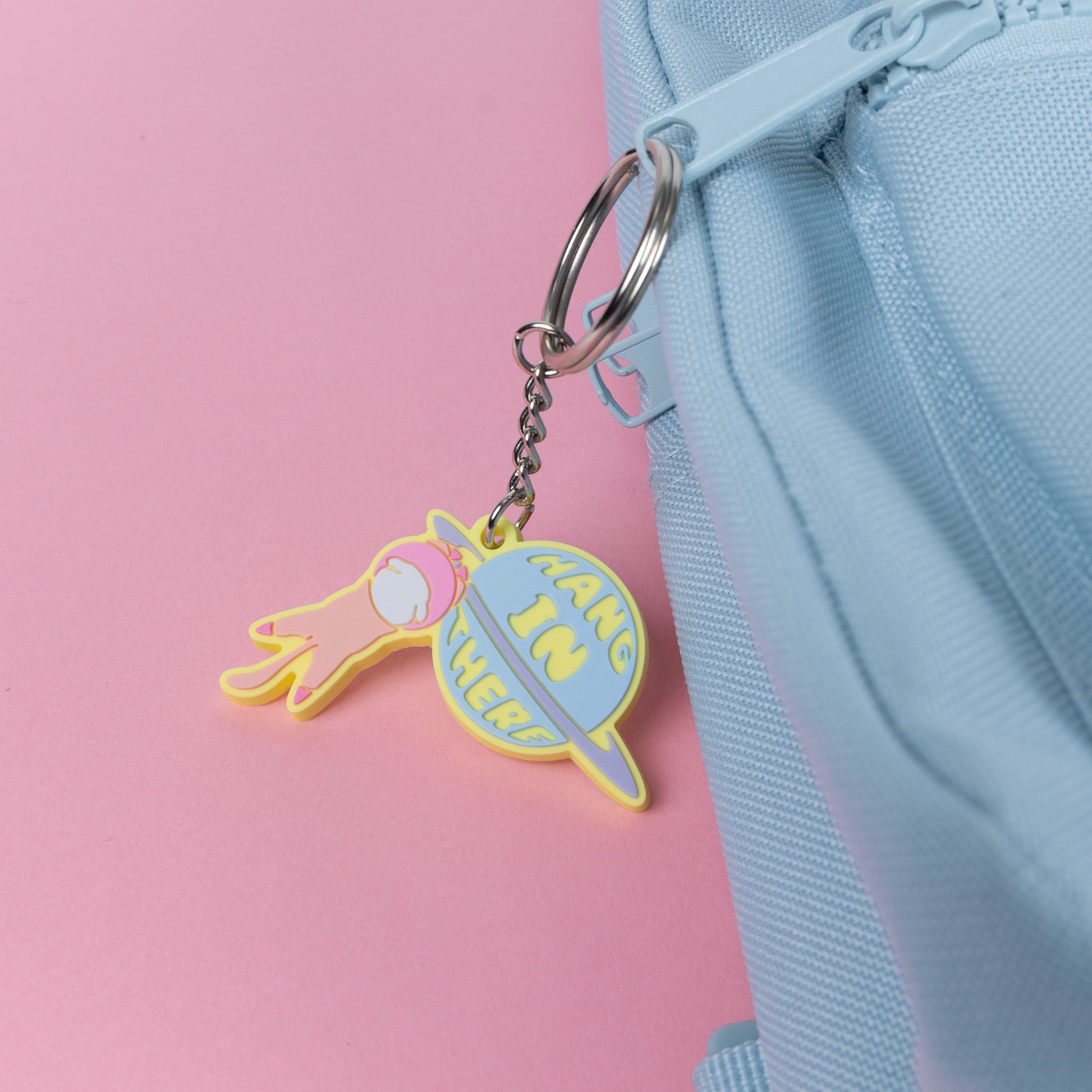 Photograph of Cute Cat Astronaut (Catstronaut) PVC Keychain, hanging onto a planet with cute phrase 'Hang In There'; attached to a rucksack.